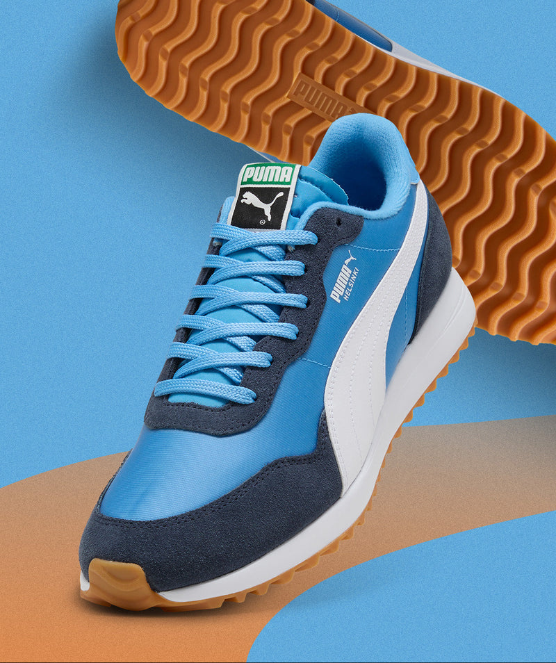 Blue and navy Puma sneaker with brown sole on a blue and orange background