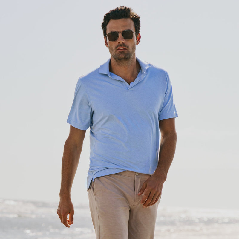 Man wearing a light blue polo shirt and beige shorts on a beach, with 'Peter Millar' branding.