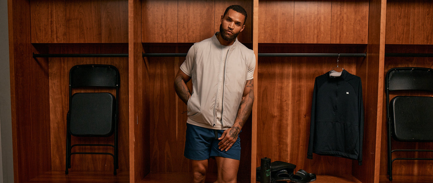 Man standing in a locker room with wooden lockers and sports equipment.